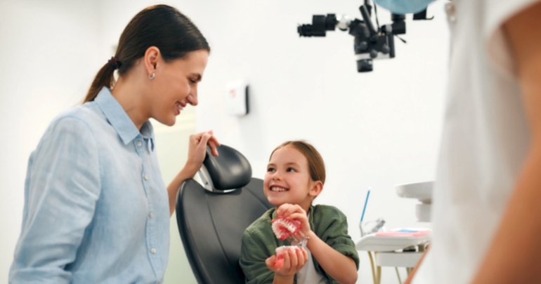 Orthodontics and children's health - child holding false teeth and gums with mother present - Gillespie Approach–Craniosacral Fascial Therapy